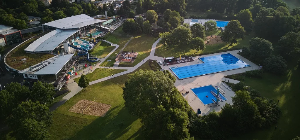 Luftaufnahme eines Schwimmbads mit mehreren Becken und Grünflächen.